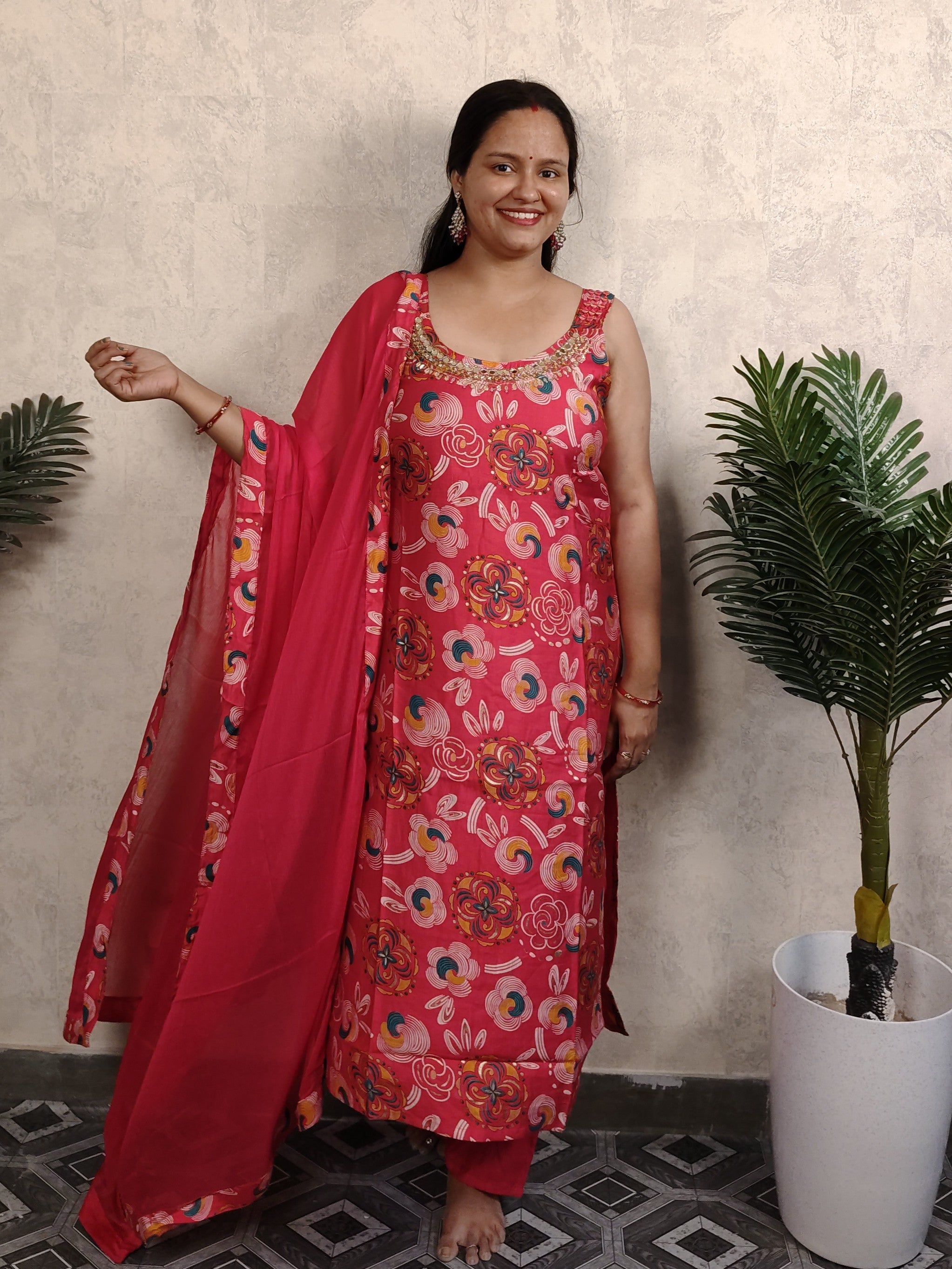 Woman in a pink floral dress standing indoors with plants in the background