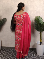 Woman in a pink saree with floral patterns standing against a light-colored wall.