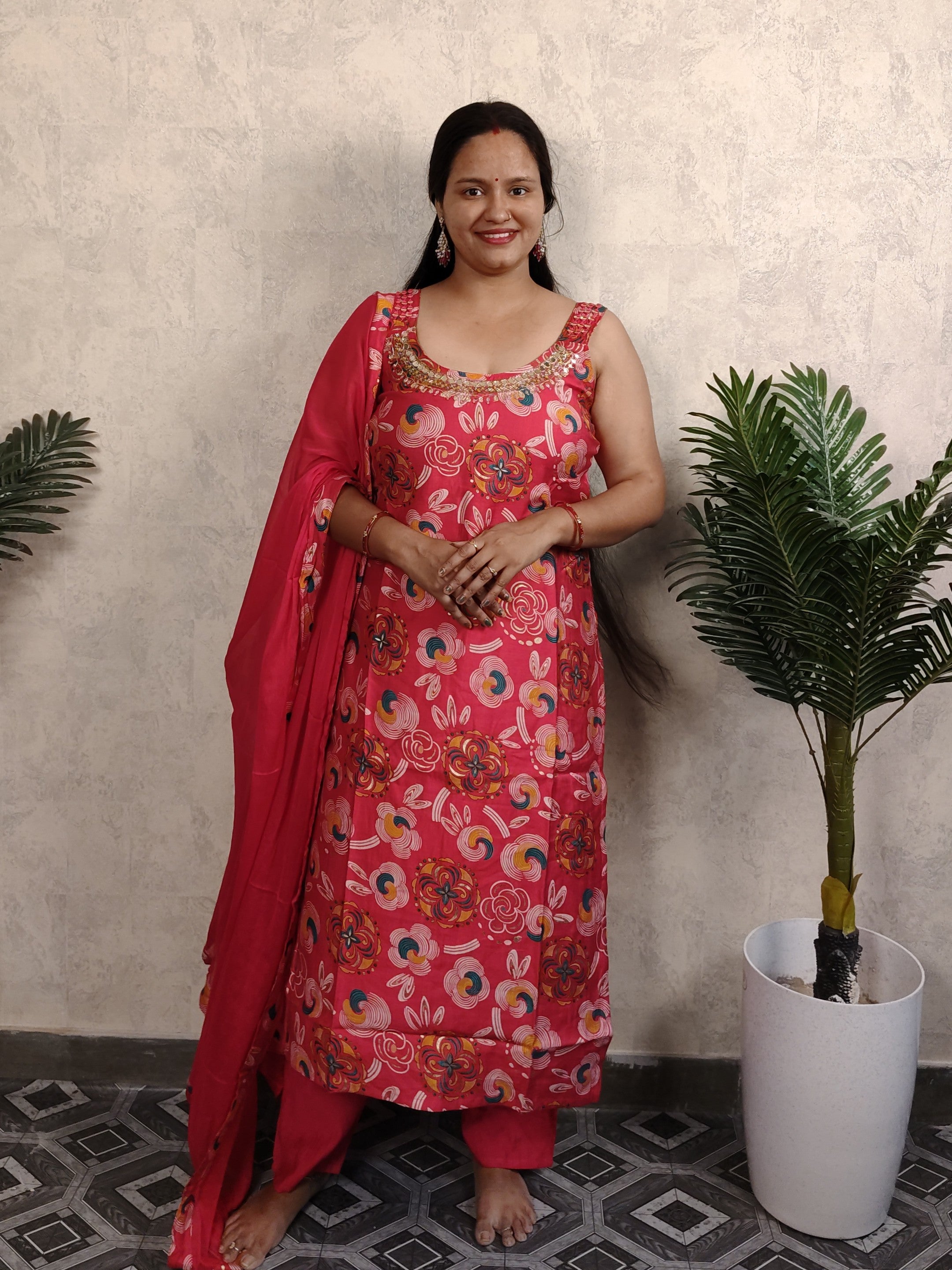 Woman in a pink floral dress standing indoors with plants in the background