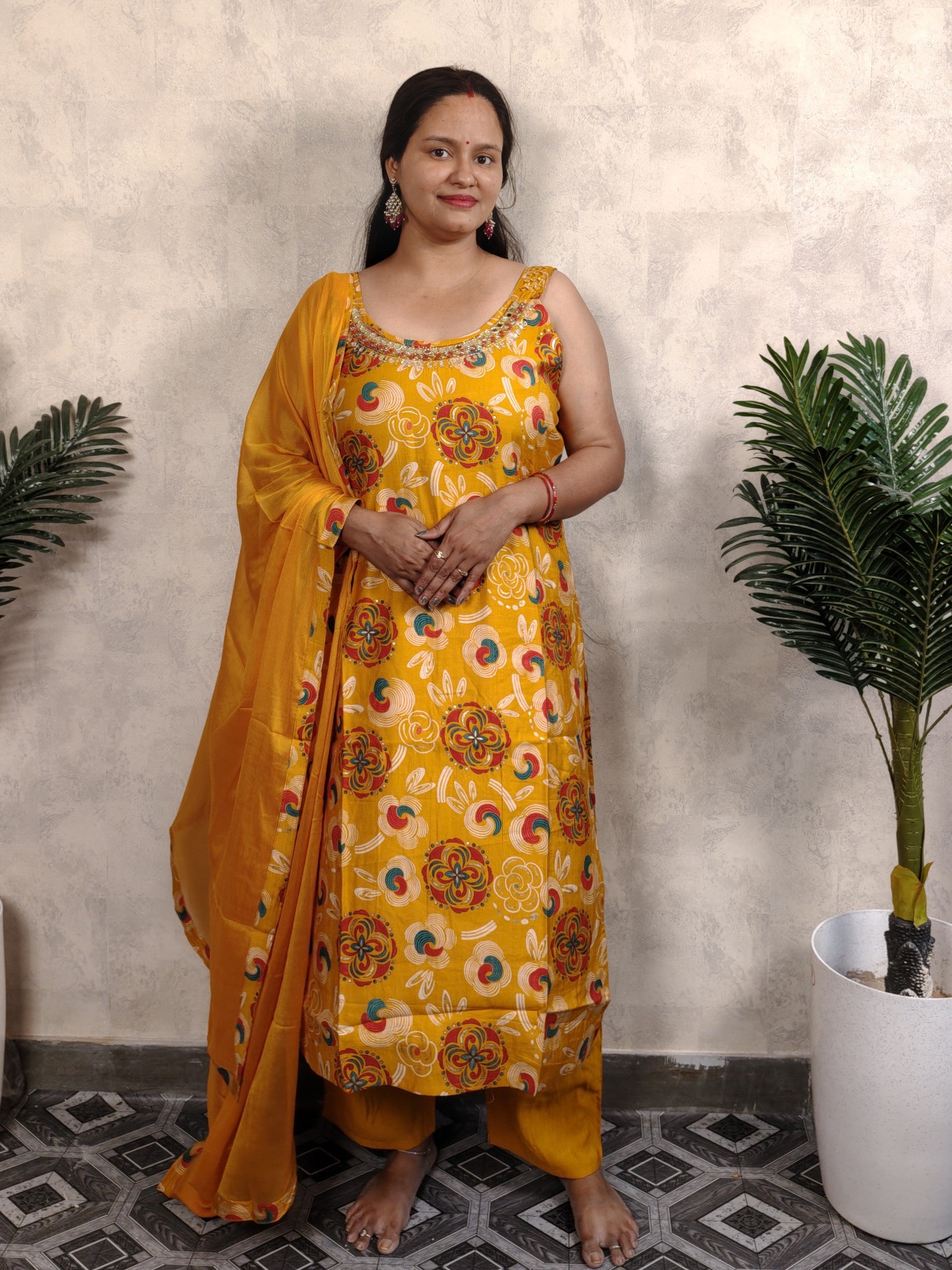 Woman in a yellow floral dress standing indoors with plants in the background